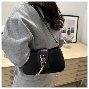 Detail of minimalist black leather shoulder bag with gold metal buckle and tassels