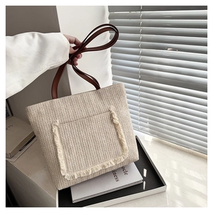 Detalle del bolso tote de paja tejida beige con bolsillo de flecos y asas de cuero café