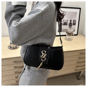 Detail view of black leather crescent bag featuring a gold S-shaped buckle and metal tassels