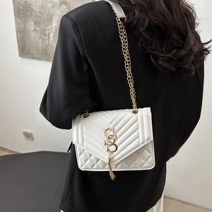 Sac bandoulière matelassé blanc avec chaîne dorée et pompon porté sur un blazer