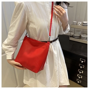 Detail of red water-resistant bucket bag with silver metal buckles on a slim shoulder strap