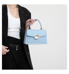 Detail of light blue handbag with crocodile texture and golden metal twist-lock closure