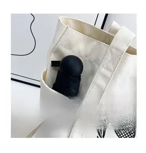 Detail of a white canvas tote bag side pocket with a compact folding umbrella inside