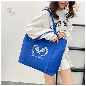 Blue canvas tote bag with Queen Tennis logo shown on shoulder of a female model