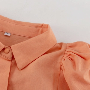 Detail der korallenfarbenen Bluse mit Reverskragen, Puffärmeln und strukturierter Baumwolle