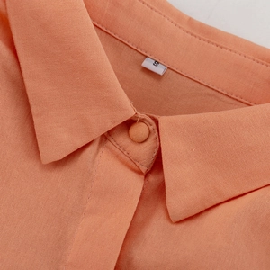 Detail eines orangefarbenen Leinenhemdkragens mit passendem Knopf und Größenetikett S