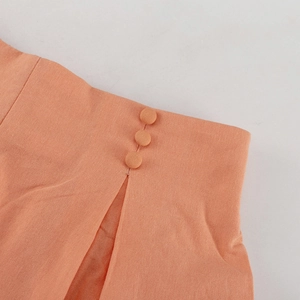 Detail der orangefarbenen Leinenhose mit stoffbezogenen Knöpfen und seitlichem Schlitz