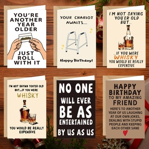 Set of 6 humorous birthday greeting cards displayed on wooden table with holiday decor