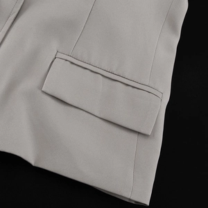 Detail view of the flap pocket and fine fabric texture on a grey tailored blazer