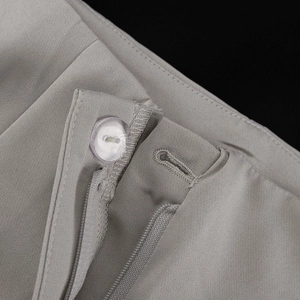 Macro detail of high-quality light gray trousers featuring a pearlescent button and zipper
