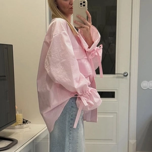 Details von rosa gestreiftem Oversize-Hemd mit ausgestellten Ärmeln und Schleifen