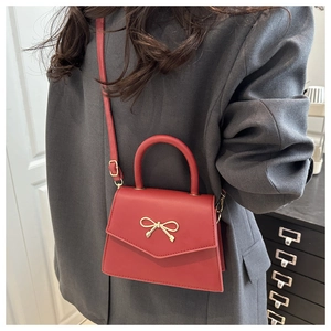 Detail view of red bow crossbody bag with gold metal buckle and adjustable strap