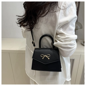 Detail of a black crossbody bag with gold bow clasp worn by model in a soft home setting