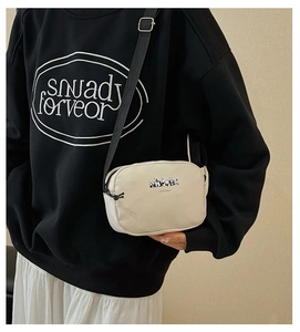 Detail of beige canvas crossbody bag with panda print, black zipper, and adjustable strap