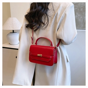 Détail du sac bandoulière rouge avec fermoir doré sur une veste blanc cassé