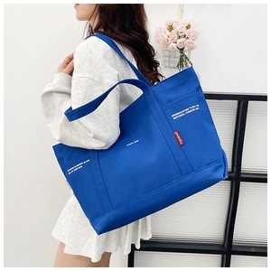 Detail of the blue canvas tote bag with white text print worn by a model in a studio