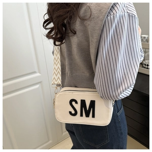 Detail of cream crossbody camera bag featuring SM logo and wide patterned shoulder strap
