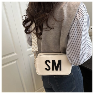 Detail of cream rectangular crossbody bag featuring black SM lettering and wide jacquard strap