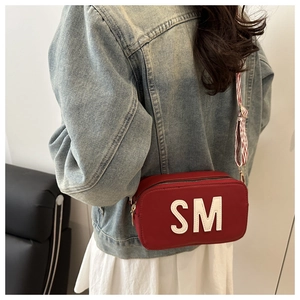 Detail of red square crossbody bag with SM print and striped woven shoulder strap