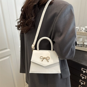 Elegant white crossbody square bag with gold bow ornament worn by a model in spring style