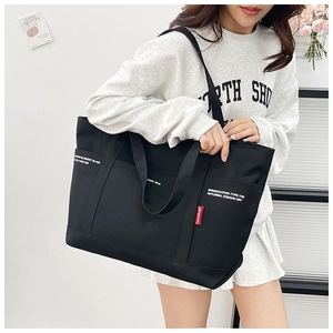 Detail of black canvas tote bag showing industrial text, outer pocket and red woven tag