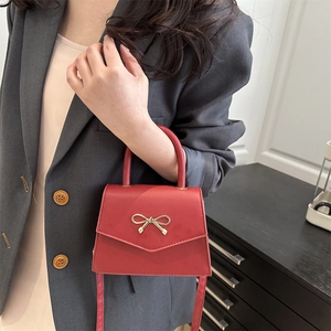 Red leather handbag with gold bow lock and crossbody strap on a grey suit model