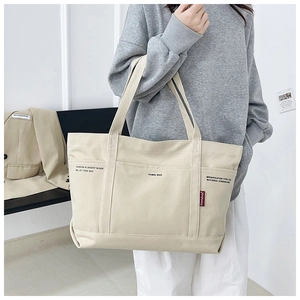 Detail of the multi-pocket canvas tote bag featuring industrial style text and red logo tag