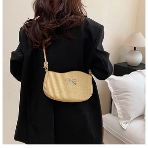 Detail of beige straw shoulder bag featuring a silver bow accent and woven rope strap