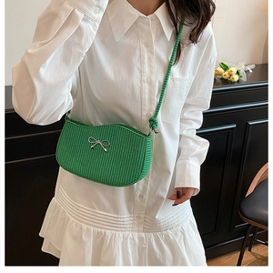Detail of green knit crossbody bag with silver bow accent on model's shoulder