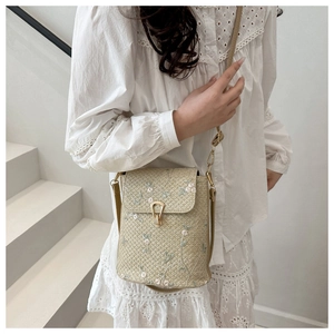 Détail du sac seau en paille tressée avec broderies florales délicates et fermoir doré chic
