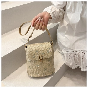 Détail du sac seau tressé beige avec broderies florales roses et fermoir métallique