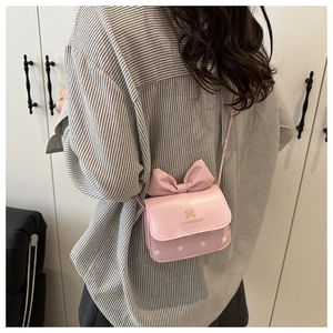 Détail du sac bandoulière rose à nœud et pois avec logo doré porté par un mannequin