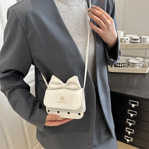 Sac bandoulière blanc minimaliste avec nœud et logo doré sur un élégant blazer gris