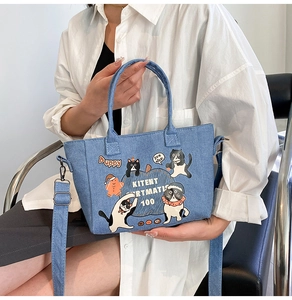 Detail of blue denim bucket bag featuring cartoon cat prints and adjustable wide shoulder strap