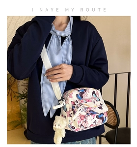 Detail of butterfly print crossbody bag featuring a plush bear charm and woven strap