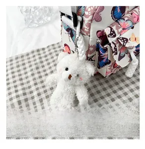 Close-up of a plush white bear charm attached to a floral shell bag with metal chain