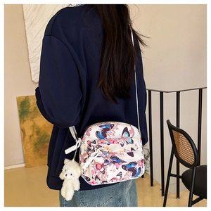 Back view of woman wearing a white floral butterfly print crossbody bag with bear charm