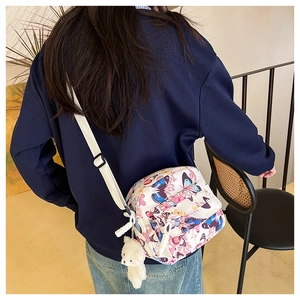 Detail of white butterfly print crossbody bag worn by model with plush bear charm accessory
