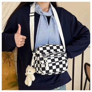 Dettaglio della borsa a tracolla a scacchi con cinturino bianco e un simpatico ciondolo a orso
