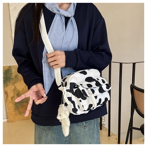 Close-up of cow print crossbody bag with plush bear charm and white canvas strap