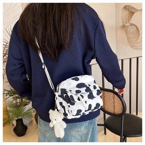 Detail view of cow print canvas crossbody bag with cute plush bear charm on strap