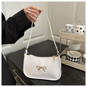 Close-up of white quilted underarm bag with gold bow accent and zip closure details