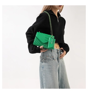 Detail of green quilted crossbody bag with metal chain strap and small coin purse attachment