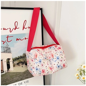 Detalle de neceser acolchado de algodón con estampado floral y correa roja audaz