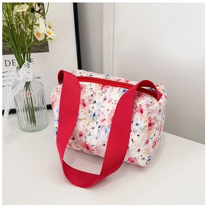 Detalle de la bolsa de maquillaje acolchada con flores y asas rojas en la mesa