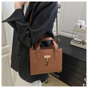 Détail du sac à main marron motif litchi avec boucle dorée et pendentif cerf élégant