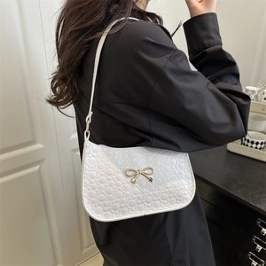 Sac sous le bras blanc avec nœud doré, porté par un mannequin dans un style moderne