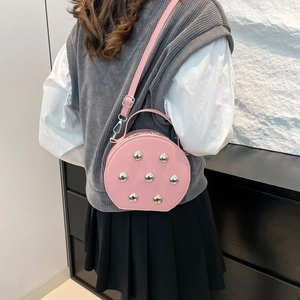 Sac bandoulière rond rose avec rivets argentés et sangle ajustable porté par un mannequin
