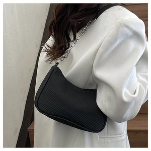 Detail of black textured underarm bag with silver chain strap on white blazer