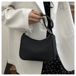 Detail of black baguette bag with woven texture and silver chain strap on model